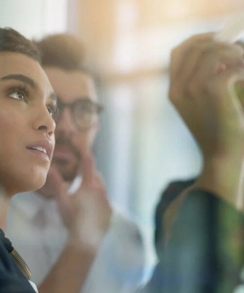 Shot of a group of colleagues brainstorming together on a glass wall in an office